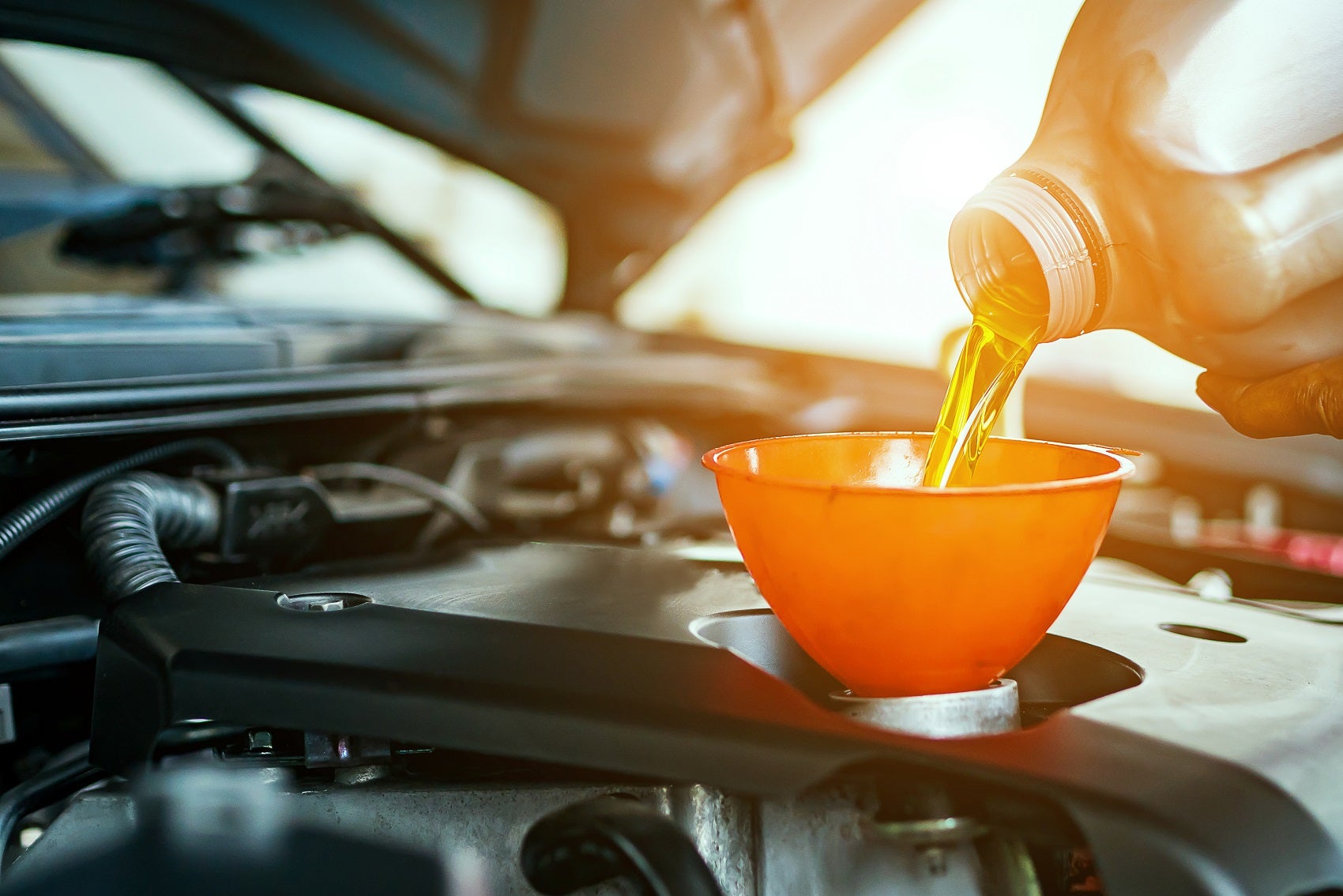 A technician pouring new synthetic engine oil into an orange oil filter as part of an oil change